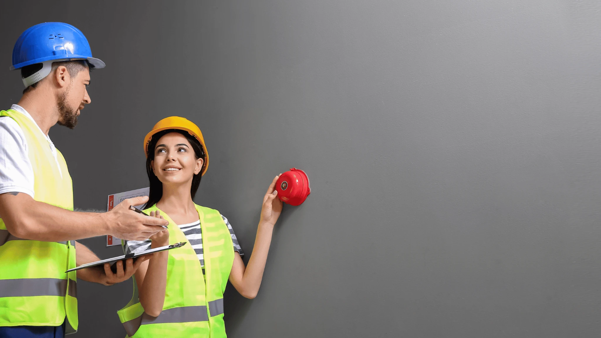 Workers in high-visibility clothing and hard hats beside a fire alarm point